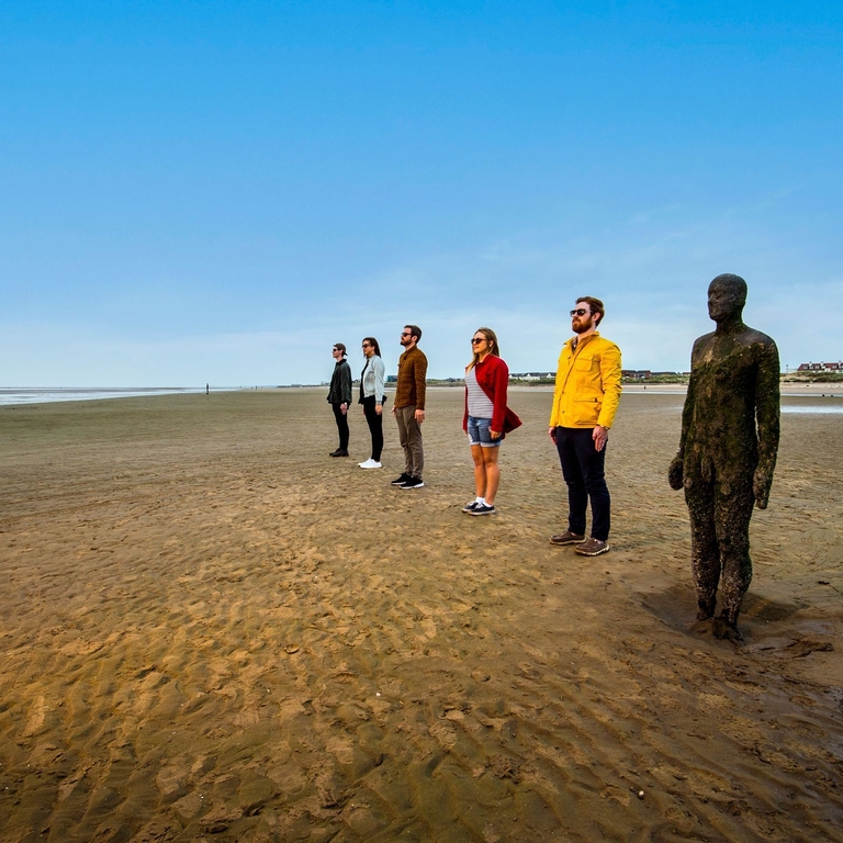 People standing beside Antony Gormley's Another Place sculptures on Crosby Beach, Liverpool