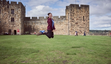 Young woman hovering on a broomstick in the Outer Bailey of Alnwick Castle