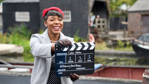 A woman smiling and holding a film board outdoors at a living museum
