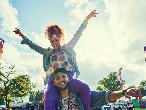 A woman sits on a mans shoulders at a festival in the summertime