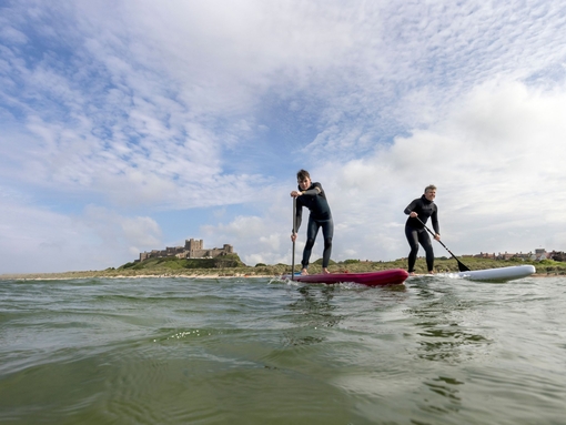 Two men on are paddleboarding in the sea with a heritage castle in the background.