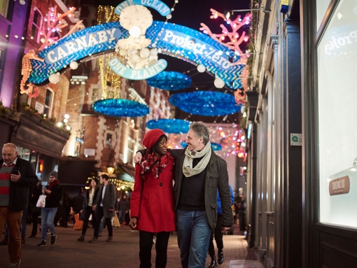 Ein Paar geht unter Weihnachtsbeleuchtung eine Straße entlang