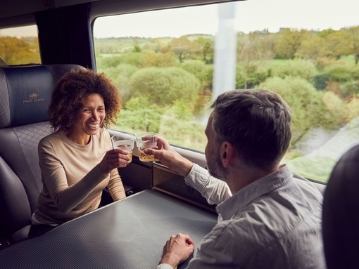 A couple enjoying a drink while travelling by train from Bath, sitting at a table, toasting