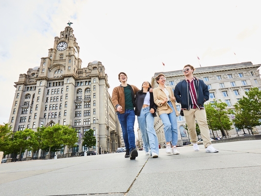 Four friends exploring a local city walking along waterfront promenade, with historic buildings in the background
