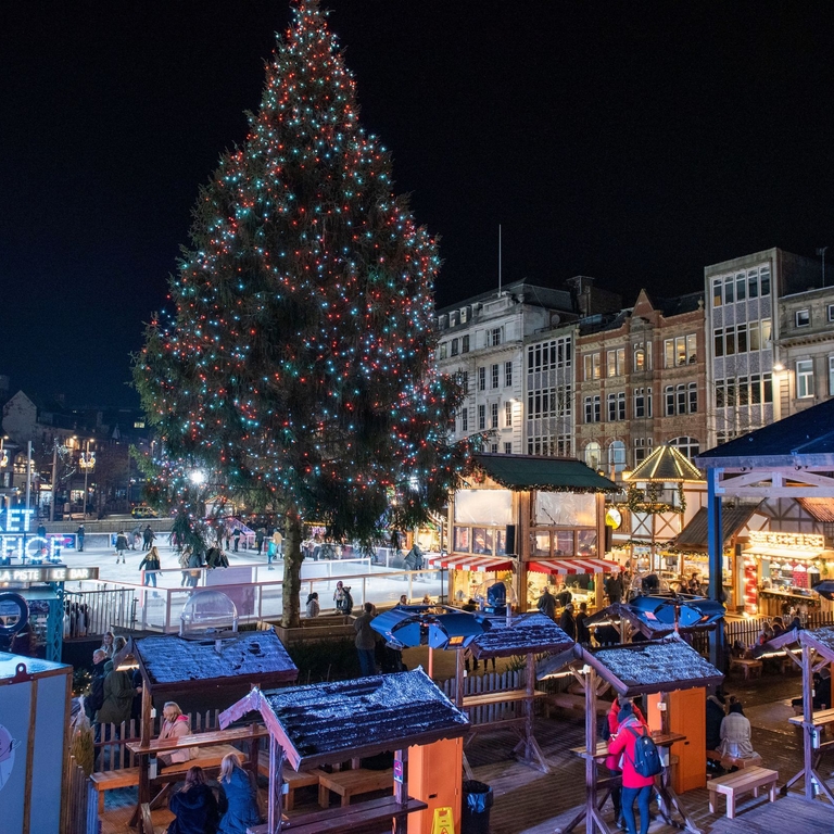 Menschen um Holzhütten und ein beleuchteter Helter Skelter im Hintergrund auf dem Weihnachtsmarkt in Nottingham