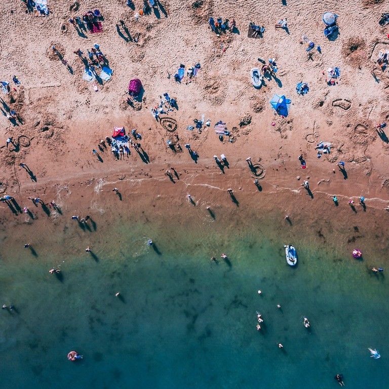 Aerial view of people on sandy beach and swimming in sea