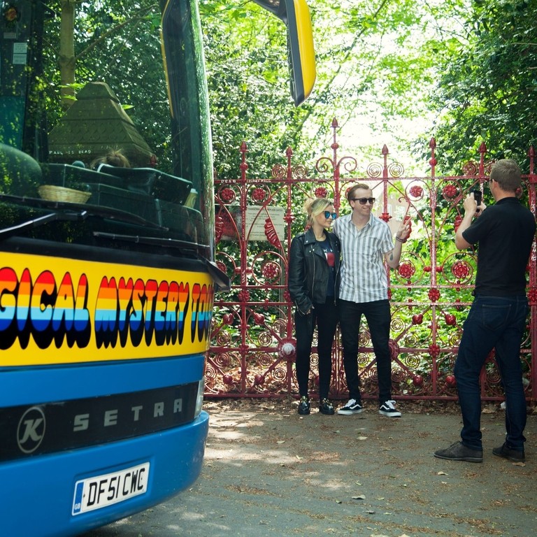 People pose for photo in front of gates on the Magical Mystery Tour in Liverpool