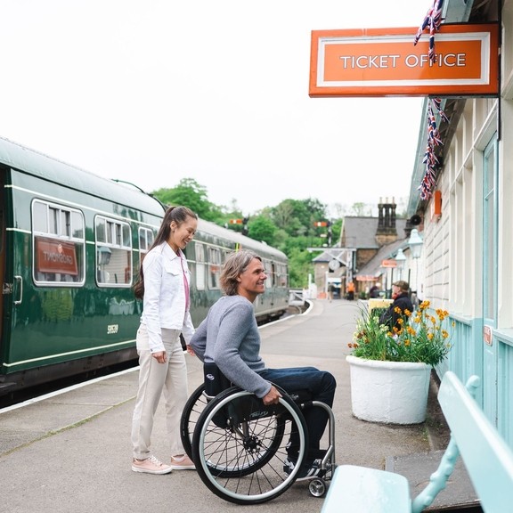 Man using a wheel chair and woman about to go into the ticket office of Grosmont Station