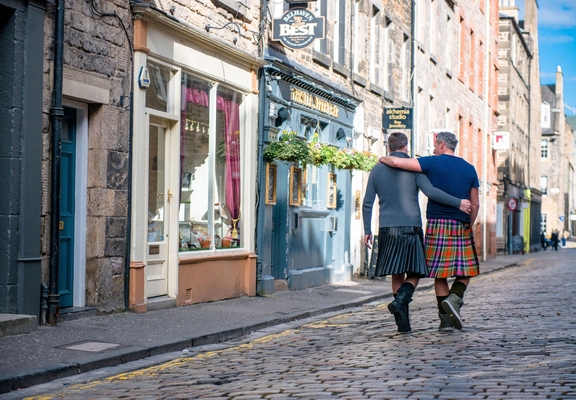 Gleichgeschlechtliches männliches Paar in Schottenröcken geht Arm in Arm