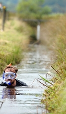 A competitor neck deep in a water-filled trench.