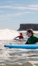 Two women hold onto surf boards waiting for waves in the sea