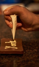 Person decorating dark chocolate with white chocolate piping