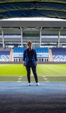 Woman standing in front of the pitch at the Manchester City Academy Stadium