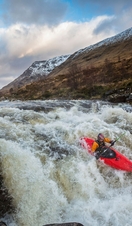 Kayaker, in a red kayak, going over raging rapids