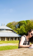A person sitting at a bench writing outside Aberystwyth Arts Centre