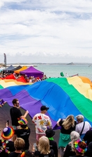 A crowd of people holding a large Pride flag on the coast in Cornwall