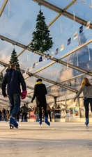 People ice skating on a skating rink under glass ceiling