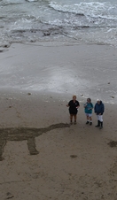 People on a beach with a dinosaur carved into the sand