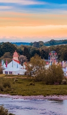 Tents and fairground rides of a summer festival beside a river.