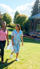 Two women walking on grass past a pergola