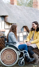 Wheelchair user and friend sat beside a wooden sculpture