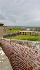A brick defensive wall with a small tower amid a larger stone fortification under grey skies.