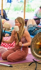 A woman on a yoga mat holding a pair of mallets and preparing to hit a set of gongs
