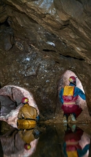A part-flooded natural cave chamber with two lead miners' tunnels blasted at the far end in Speedwell Cavern in Castleton, Derbyshire.
