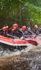 People wearing wetsuits and helmets paddling down a rapid