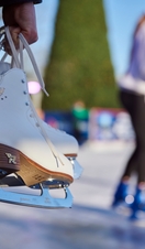 Hands holding a pair of white ice skates by the laces