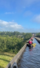 A group paddling kayaks across a viaduct with scenic views of Snowdonia/Eryri National Park