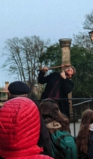 A costumed tour guide on a raised platform in front of an audience next to a historic building.