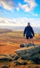 A man posing on top of Higger Tor with a wide view of the Peak District behind
