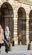 Three muslim women walking outside near stone arches