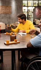 Gruppo di amici, uno dei quali in sedia a rotelle, seduto intorno a un tavolo