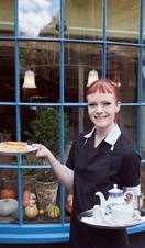 Waitress holding tray with tea and cake standing