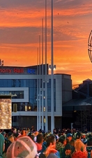 A crowd of people at a festival watching acrobats performing in the air in front of Symphony Hall, Birmingham at sunset