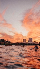 Gente en kayak por el Támesis con un cielo rojo al atardecer y los edificios de Londres al fondo