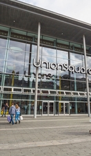 People carrying bags of shopping walking around outside of a modern shopping centre.