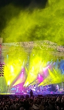 A crowd of people in front of the stage of a musical festival at night.