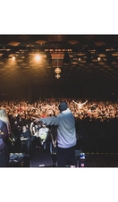 Two musicians on stage looking out to a large crowd of people dancing to the music and under bright lights and discoballs at Barrowland Ballroom in Glasgow