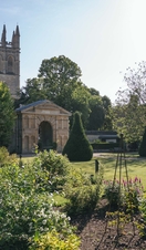 Flower bed in front of a georgian arch and building of Oxford Botanic Garden with church tower behind against blue sky