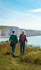 Una mano posando una pila de piedras en la costa con las Siete Hermanas al fondo