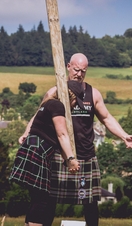 Woman wearing a kilt learning how to toss the caber with male instructor