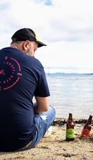 A man sat on a beach next to bottles of Snowdon Craft Beer