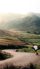 Man skateboarding down valley paths. Green landscape