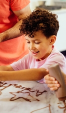 A boy, with curly hair, squeezing chocolate out of a bottle