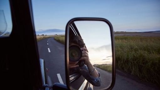 Spiegelung eines Mannes mit Kamera im Seitenspiegel eines Autos