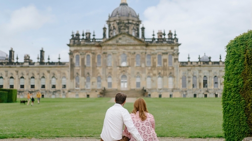 A man and a woman sit on a step looking towards a heritage building