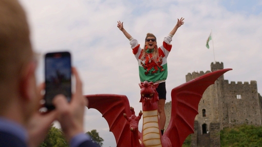 Woman has picture taken standing on a model Welsh dragon.